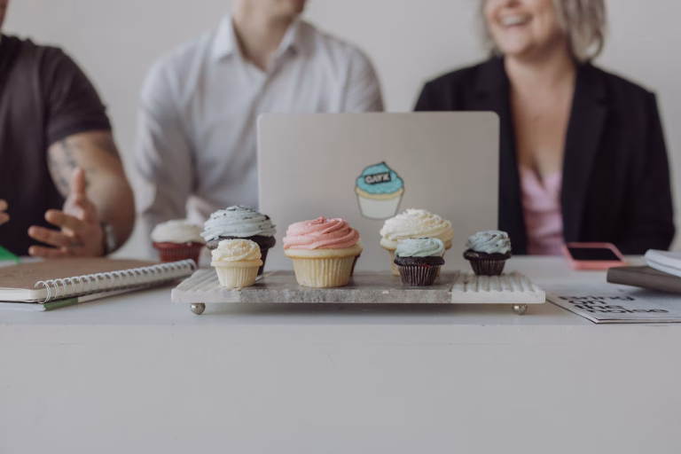 A creative team discussing ideas for a holiday marketing campaign with cupcakes and laptops on the table, symbolizing festive branding and collaboration.