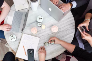 Overhead view of a marketing team collaborating around a table with laptops and planners, discussing how to move away from short-term marketing budgets toward a sustainable long-term growth strategy.