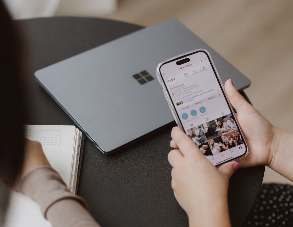 Person using smartphone to browse a responsive interface, illustrating mobile website design alongside a laptop on a desk.